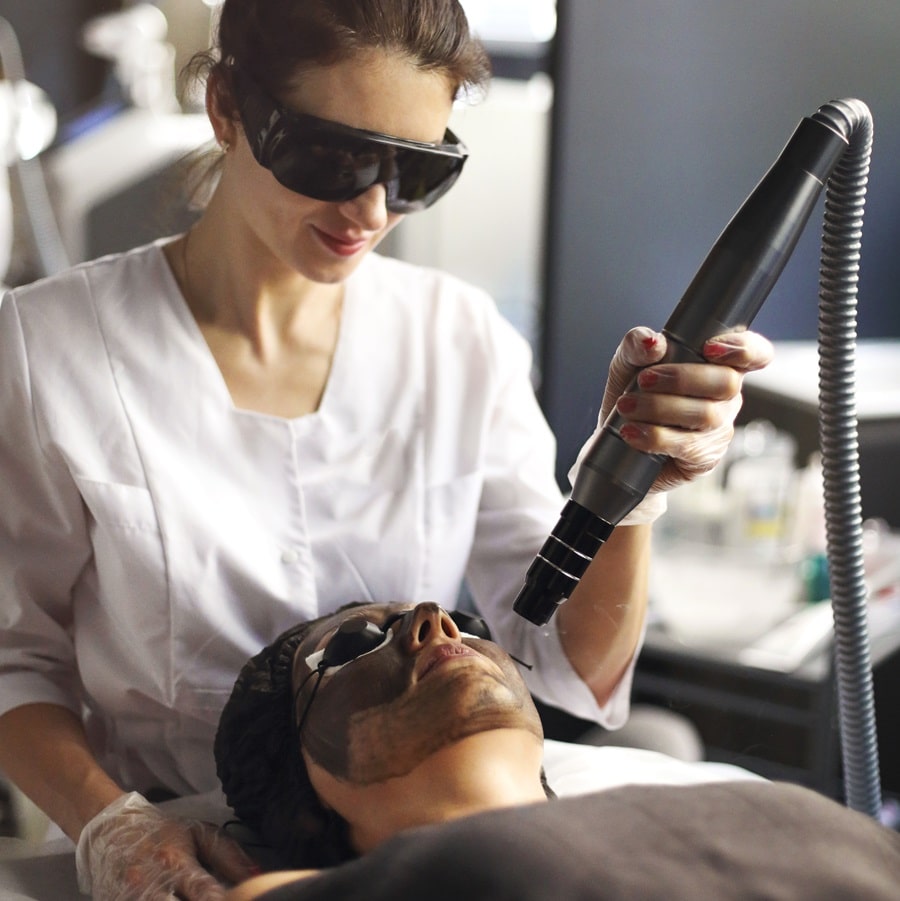 Beautician holding beauty laser near woman face covered with car